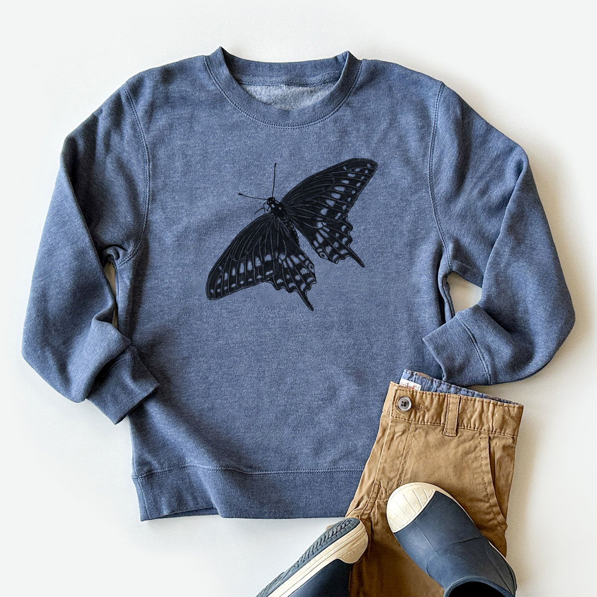 Youth crewneck sweatshirt printed with a detailed black ink illustration of a black swallowtail butterfly with its wings spread, styled flat with khaki pants and shoes.