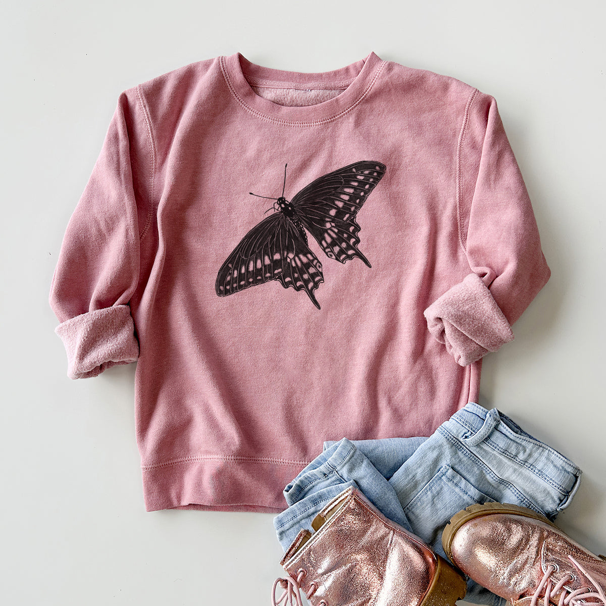 Youth crewneck sweatshirt printed with a detailed black ink illustration of a black swallowtail butterfly with its wings spread, styled flat with jeans and boots.