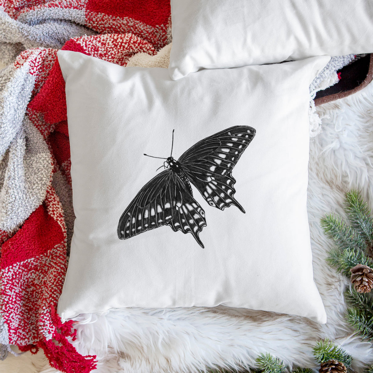 White pillow cover printed with a detailed black ink illustration of a black swallowtail butterfly with its wings spread, on a woven chair.