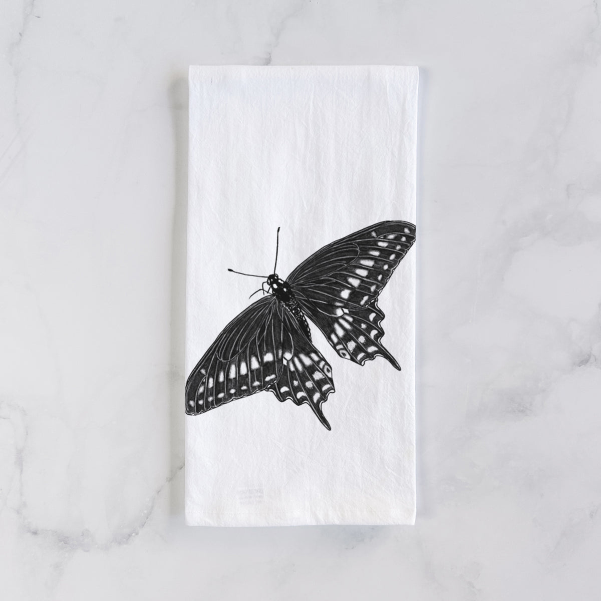 White cotton tea towel laid flat on marble, printed with a detailed black ink illustration of a black swallowtail butterfly with its wings spread.
