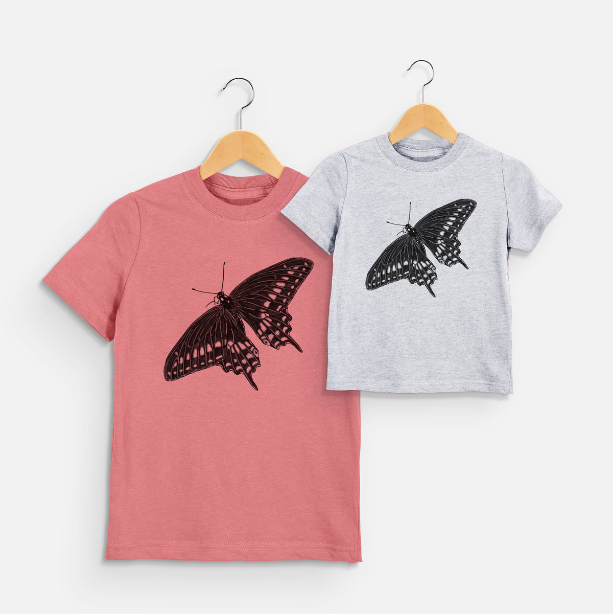Two youth t-shirts in different colors on hangers, printed with a detailed black ink illustration of a black swallowtail butterfly with its wings spread.
