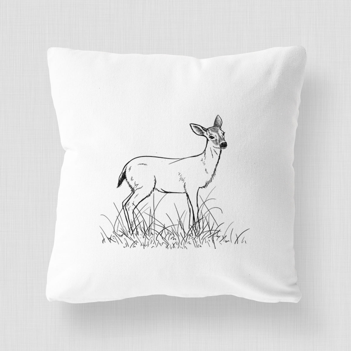 White pillow cover printed with a black ink sketch of a black-tailed deer standing in tall grass.