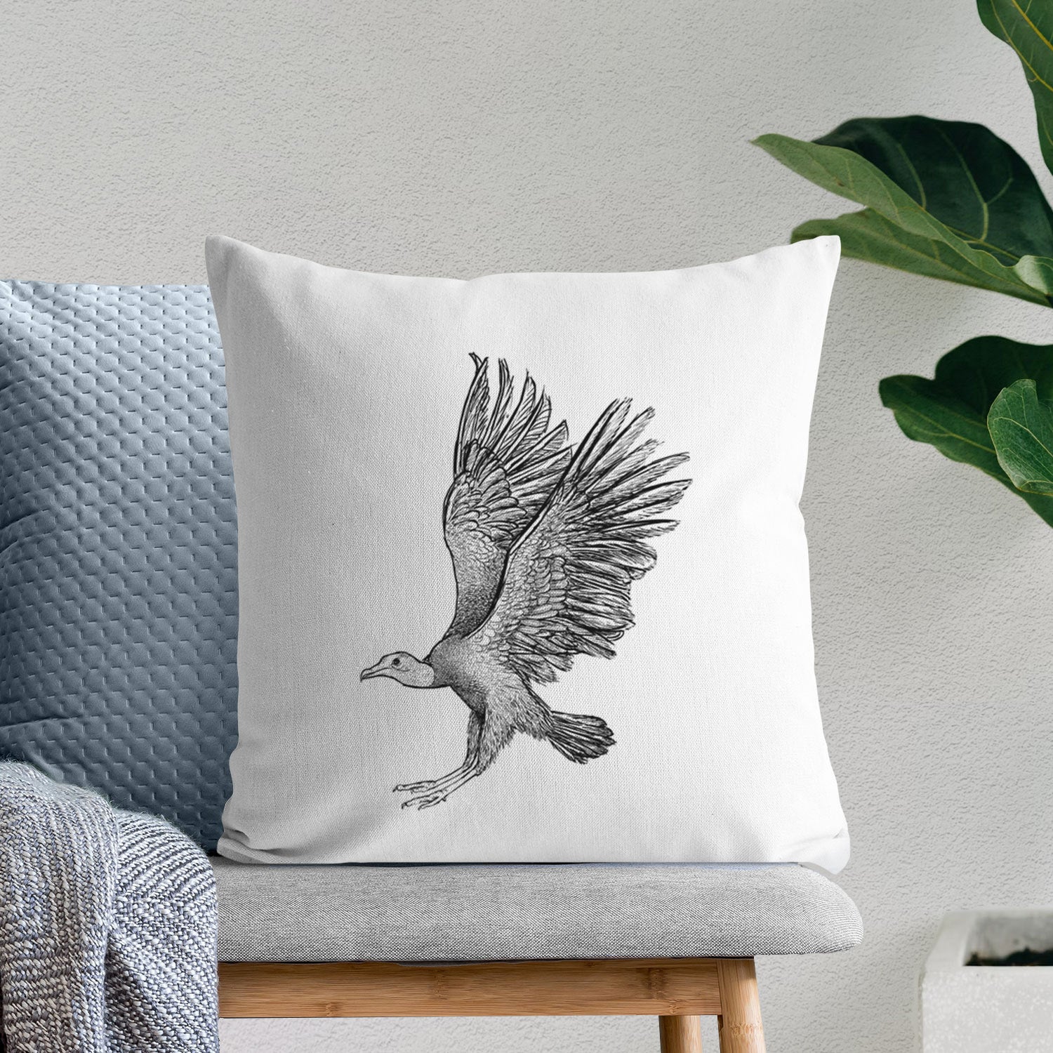White pillow cover printed with a detailed black ink illustration of a black vulture landing with its wings spread, on a bench beside plants.