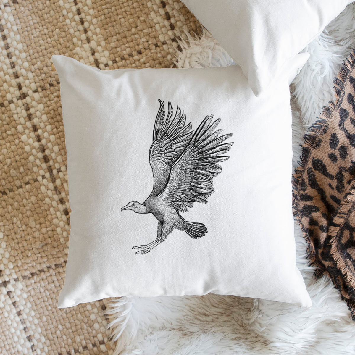 White pillow cover printed with a detailed black ink illustration of a black vulture landing with its wings spread, on a woven chair.
