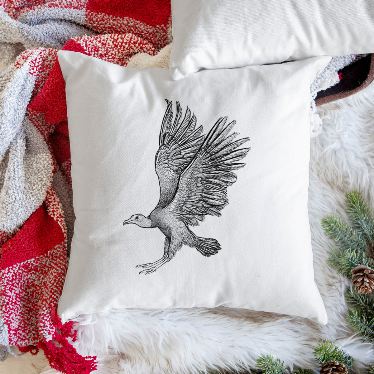 White pillow cover printed with a detailed black ink illustration of a black vulture landing with its wings spread, on a woven chair.