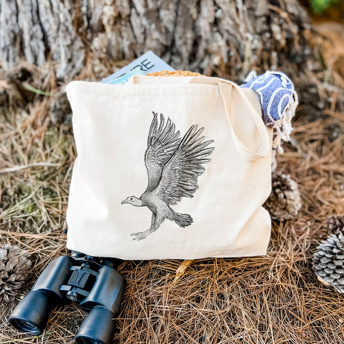 Canvas tote bag printed with a detailed black ink illustration of a black vulture landing with its wings spread, resting on dry grass beside a pair of binoculars.