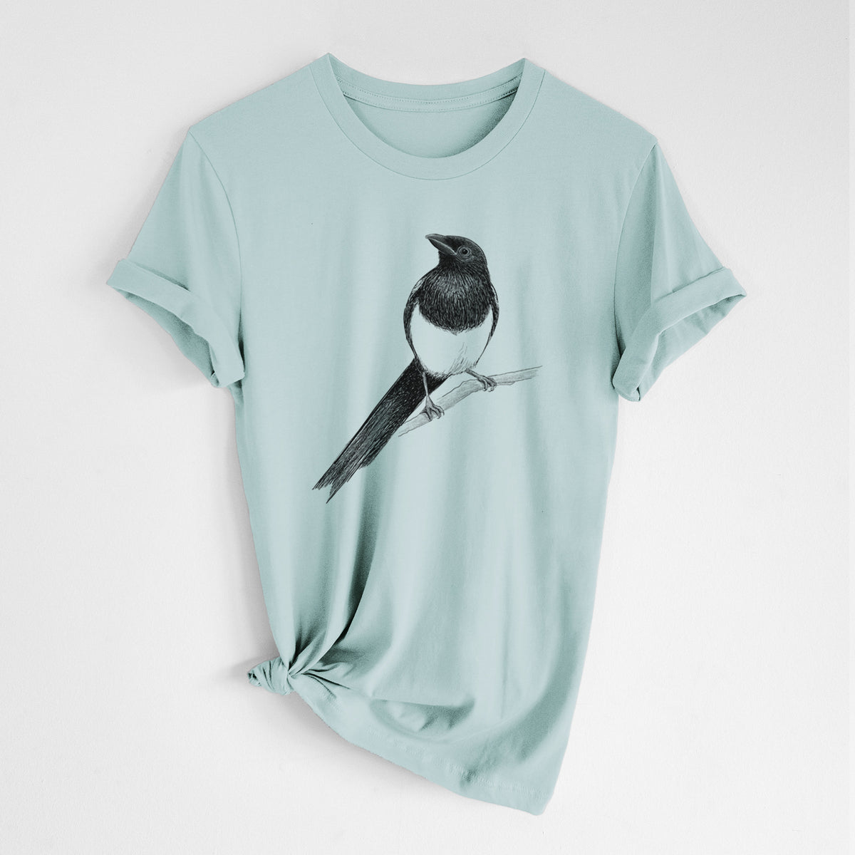 Dusty blue lightweight cotton t-shirt laid flat with the sleeves rolled, printed with a detailed black ink sketch of a black-billed magpie perched on a branch with its long tail.