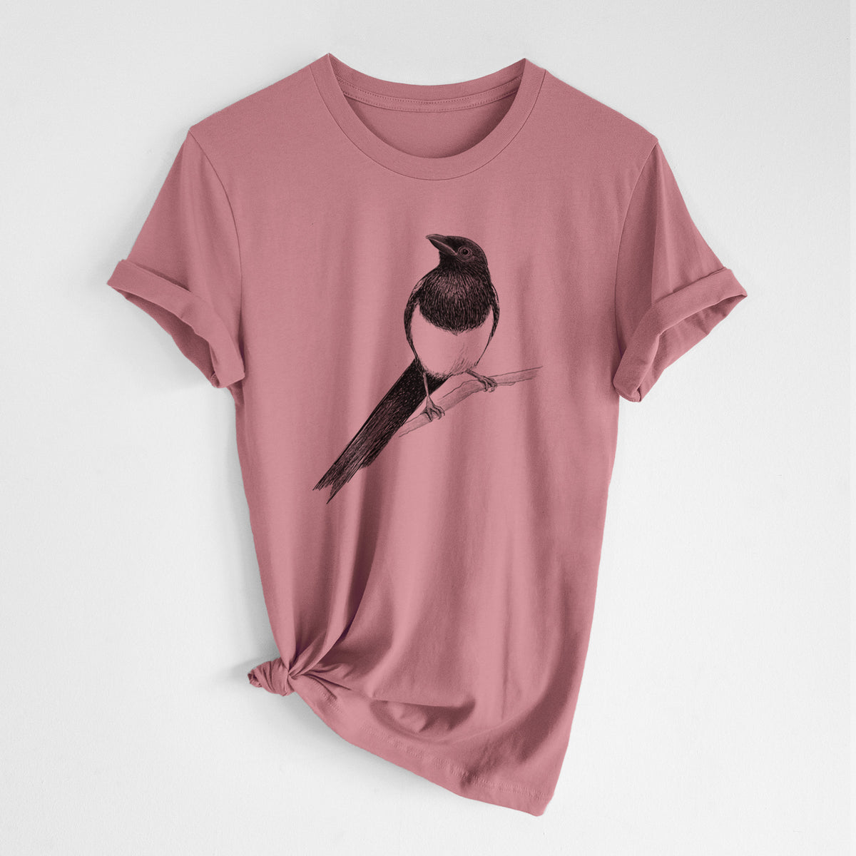 Mauve pink lightweight cotton t-shirt laid flat with the sleeves rolled, printed with a detailed black ink sketch of a black-billed magpie perched on a branch with its long tail.