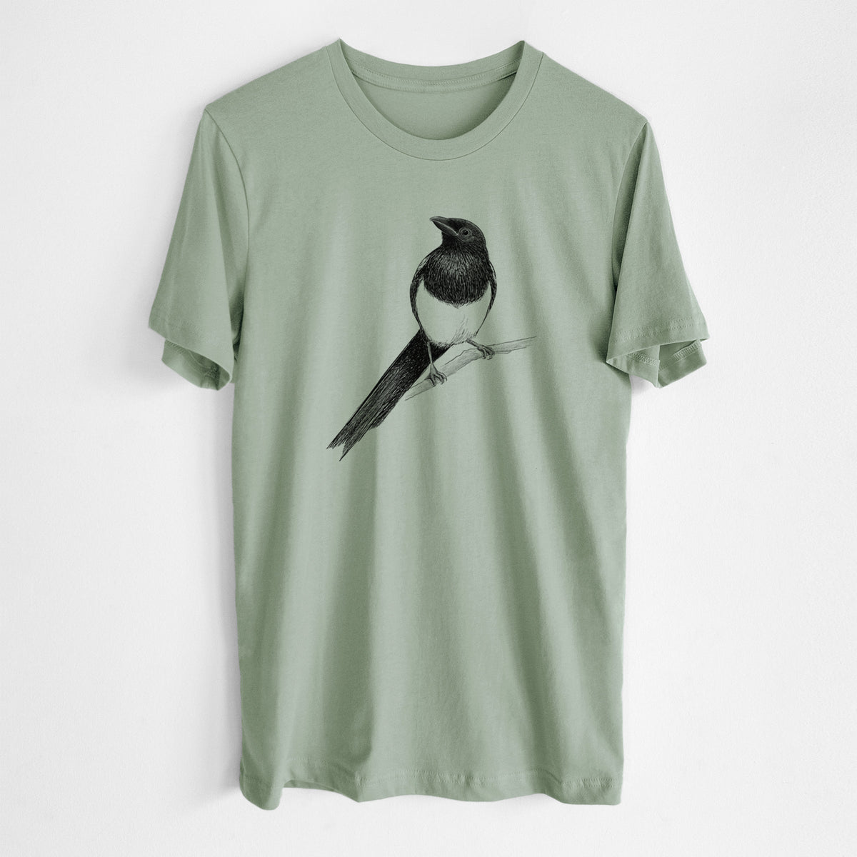 Sage green lightweight cotton t-shirt laid flat, printed with a detailed black ink sketch of a black-billed magpie perched on a branch with its long tail.