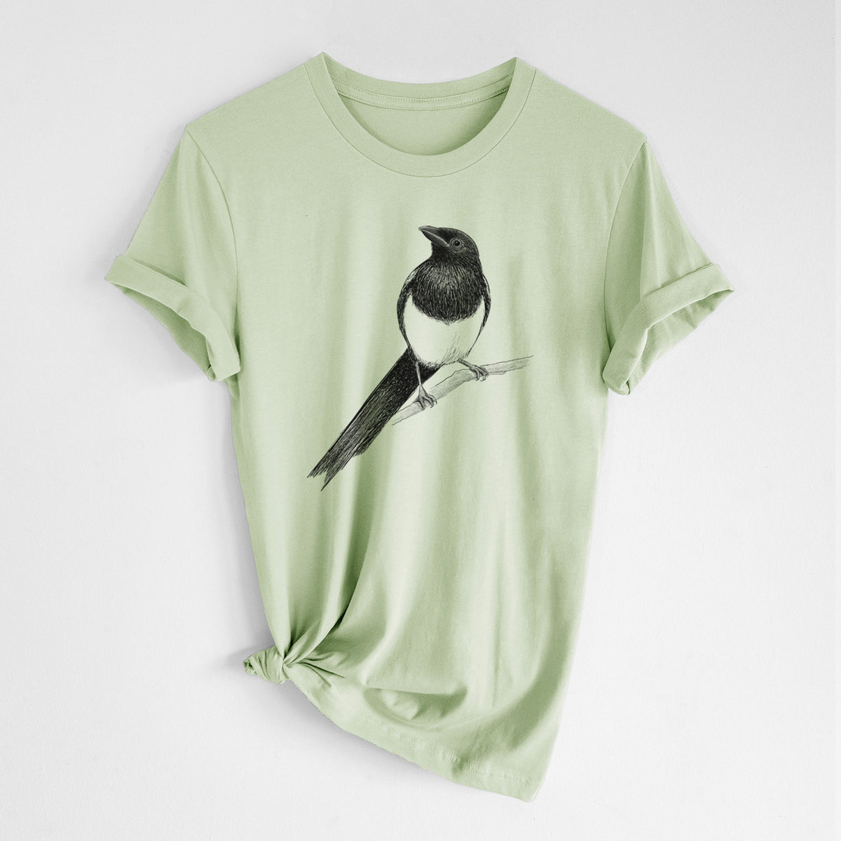 Spring green lightweight cotton t-shirt laid flat with the sleeves rolled, printed with a detailed black ink sketch of a black-billed magpie perched on a branch with its long tail.
