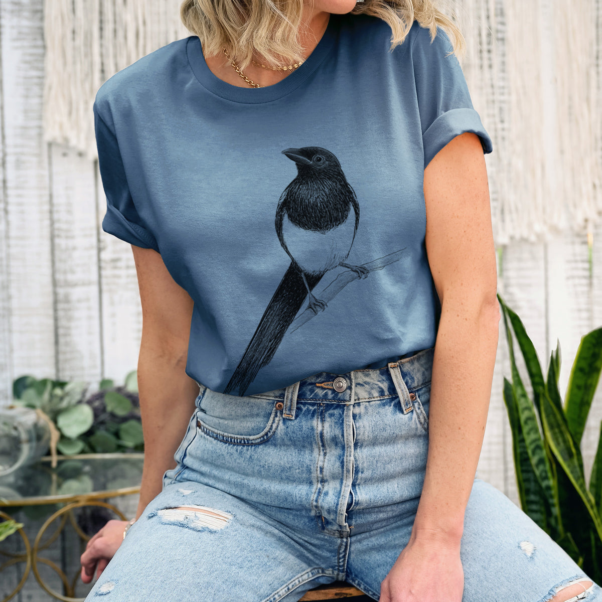 Woman wearing a steel blue lightweight cotton t-shirt printed with a detailed black ink sketch of a black-billed magpie perched on a branch with its long tail.