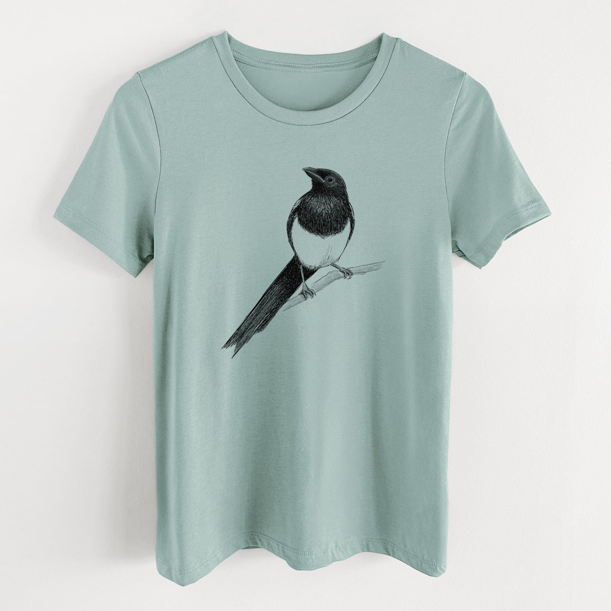 Dusty blue women's relaxed fit cotton t-shirt laid flat, printed with a detailed black ink sketch of a black-billed magpie perched on a branch with its long tail.
