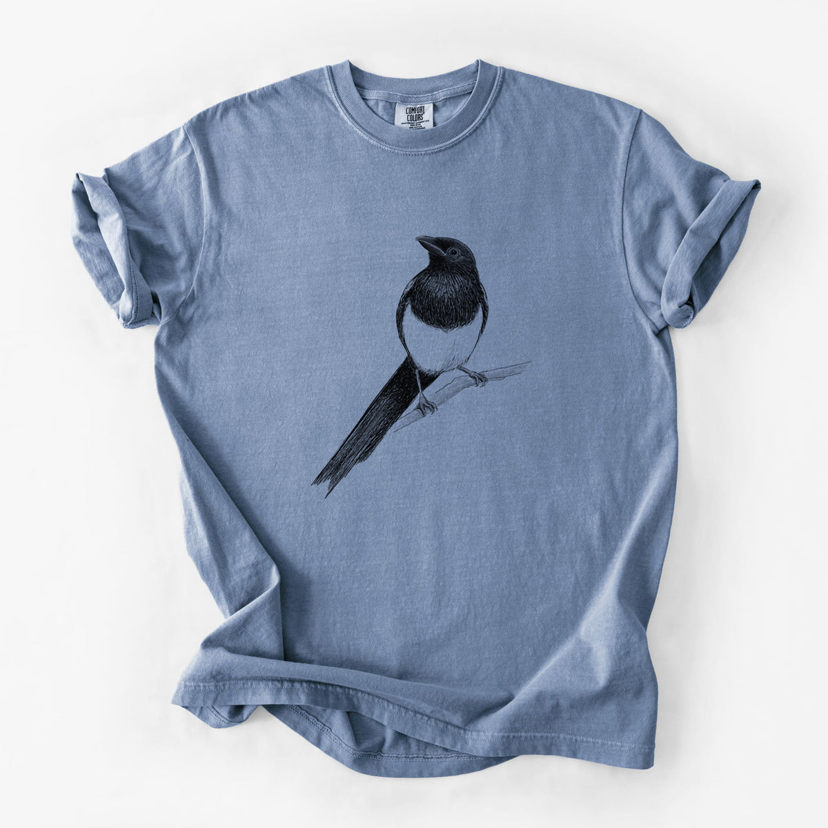 Blue jean Comfort Colors t-shirt laid flat, printed with a detailed black ink sketch of a black-billed magpie perched on a branch with its long tail.