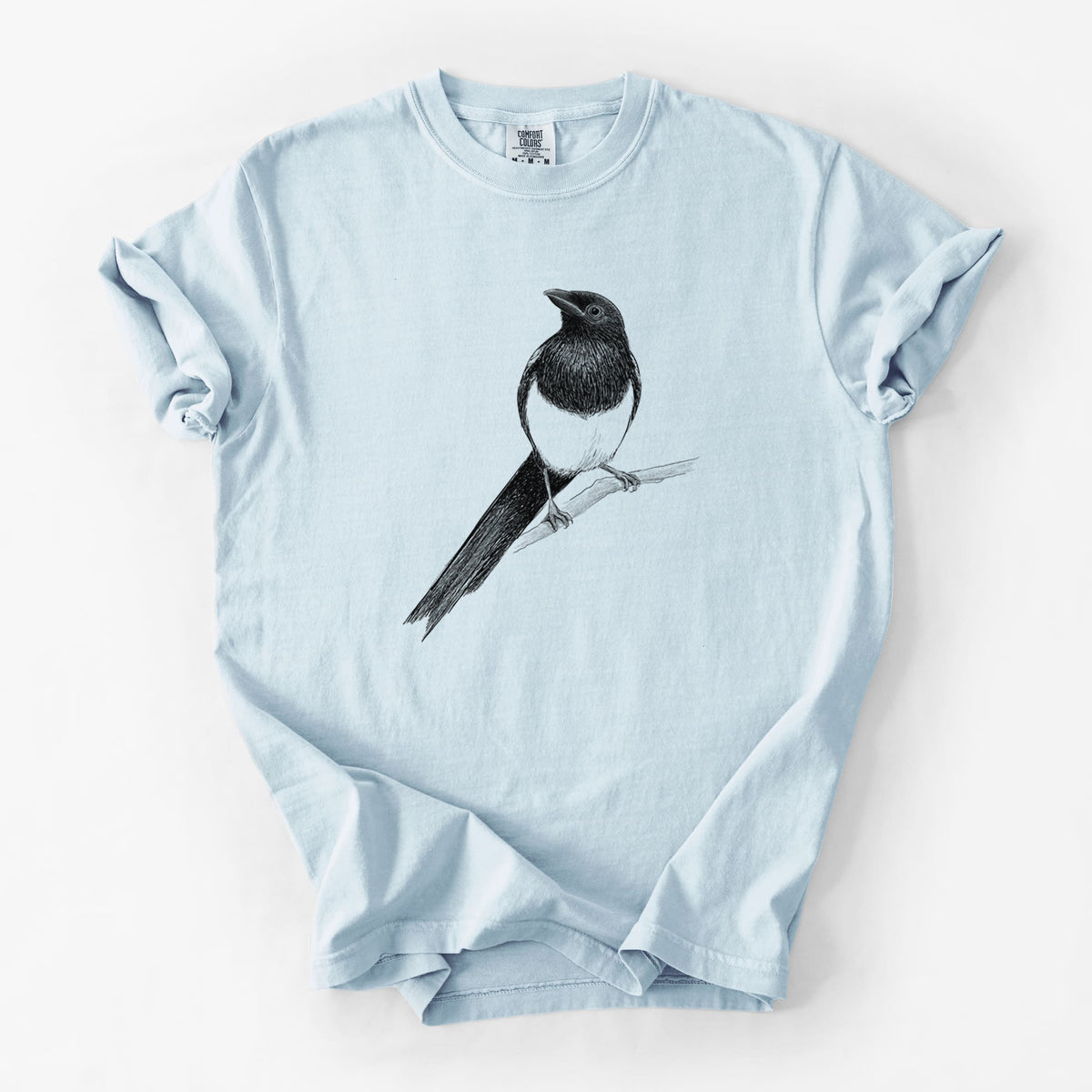 Chambray blue Comfort Colors t-shirt laid flat, printed with a detailed black ink sketch of a black-billed magpie perched on a branch with its long tail.