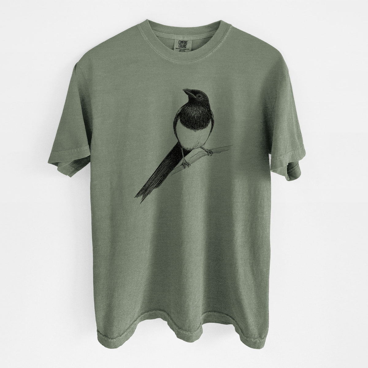 Moss green Comfort Colors t-shirt laid flat, printed with a detailed black ink sketch of a black-billed magpie perched on a branch with its long tail.