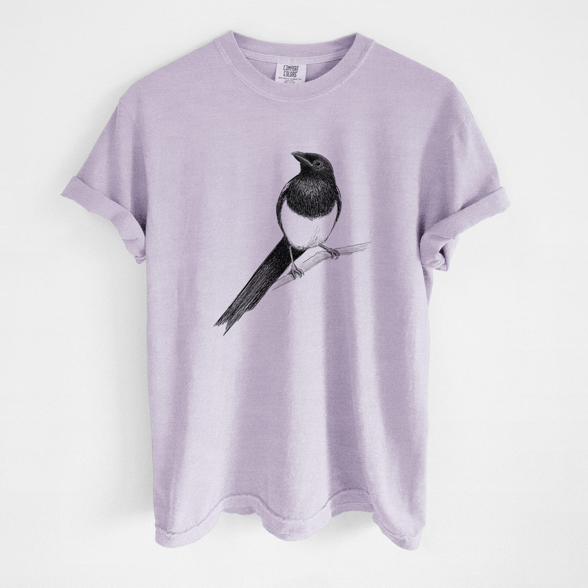 Orchid purple Comfort Colors t-shirt laid flat, printed with a detailed black ink sketch of a black-billed magpie perched on a branch with its long tail.