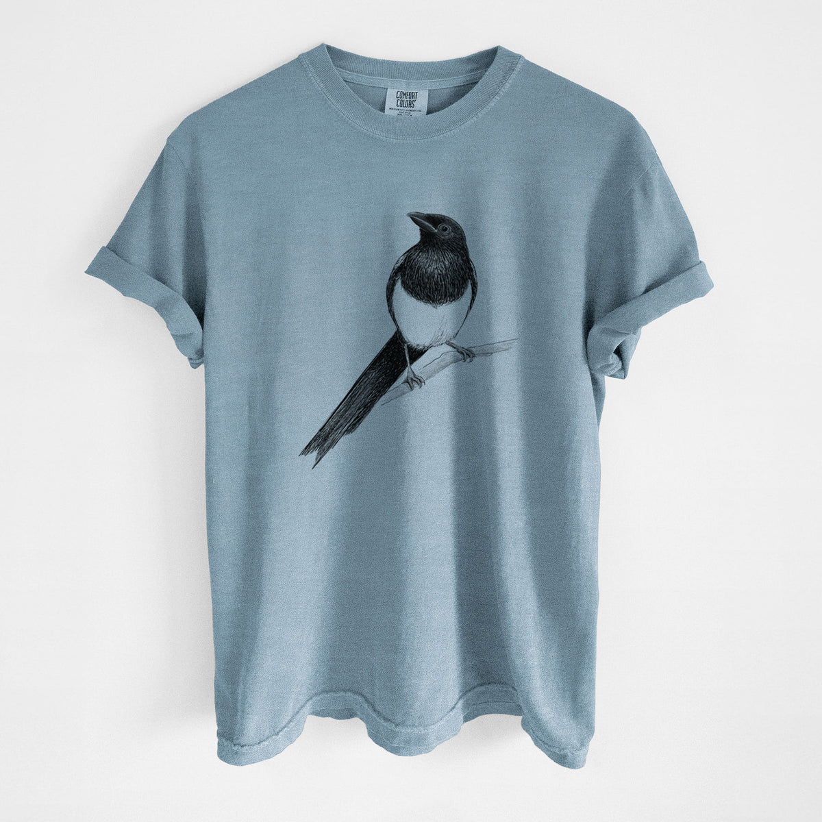 Steel blue Comfort Colors t-shirt laid flat, printed with a detailed black ink sketch of a black-billed magpie perched on a branch with its long tail.