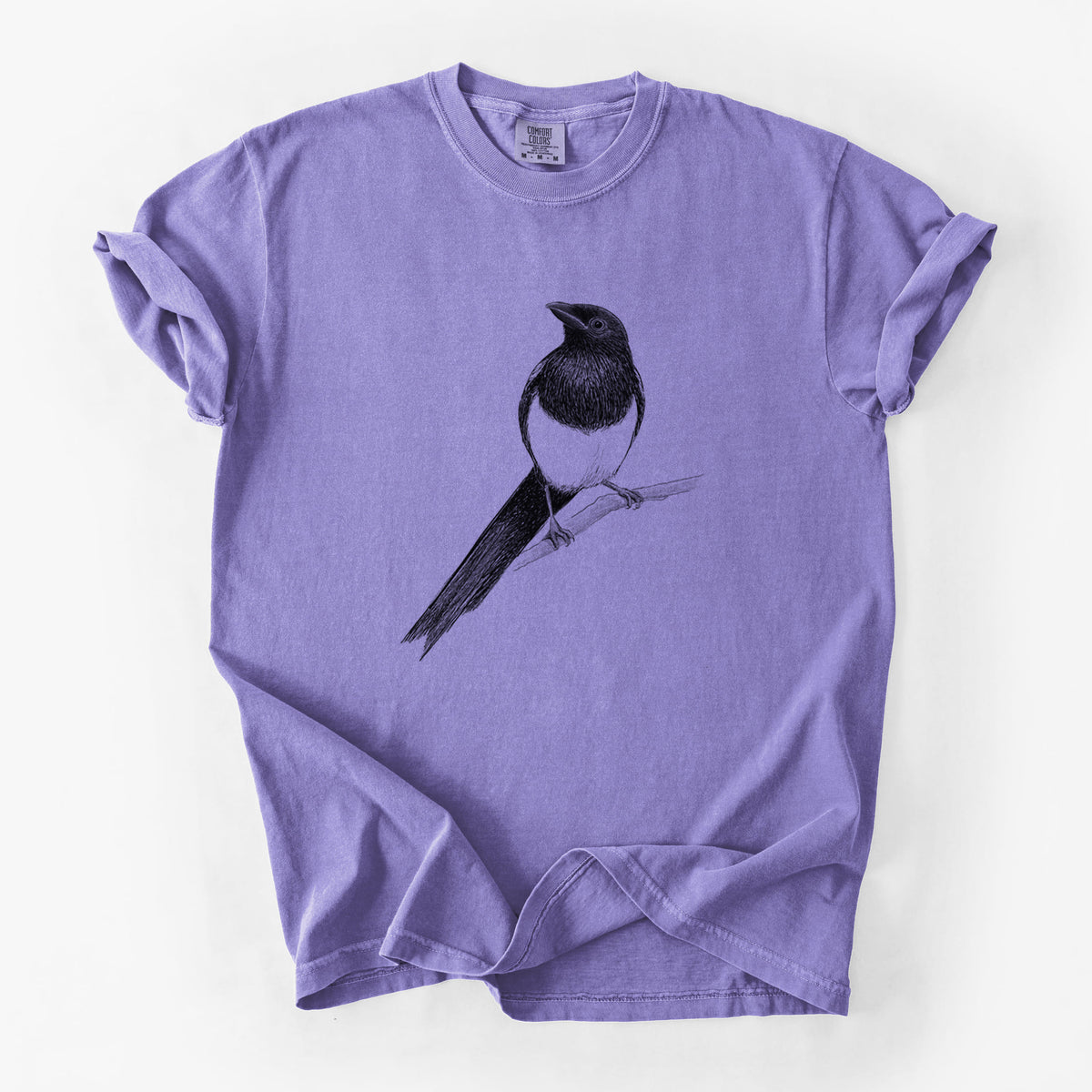 Violet purple Comfort Colors t-shirt laid flat, printed with a detailed black ink sketch of a black-billed magpie perched on a branch with its long tail.