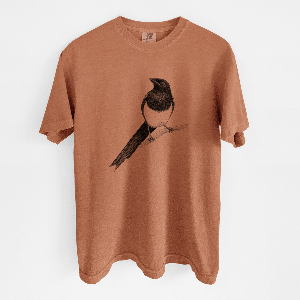 Yam burnt orange Comfort Colors t-shirt laid flat, printed with a detailed black ink sketch of a black-billed magpie perched on a branch with its long tail.