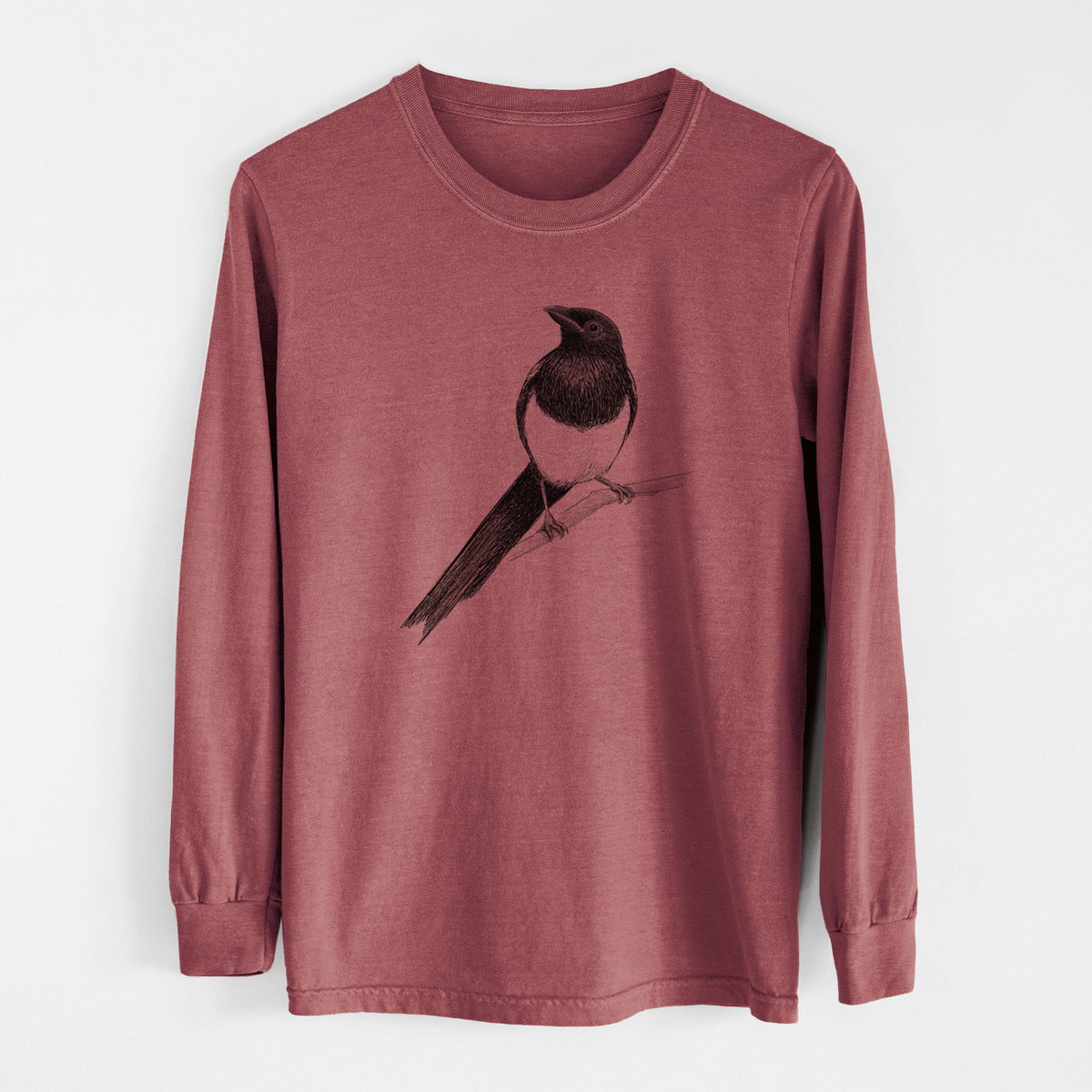 Brick red Comfort Colors long sleeve shirt laid flat, printed with a detailed black ink sketch of a black-billed magpie perched on a branch with its long tail.