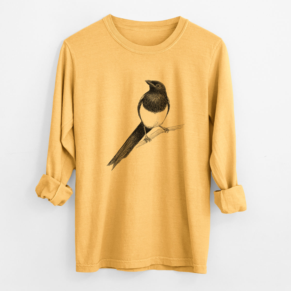 Golden wheat yellow Comfort Colors long sleeve shirt laid flat with the cuffs rolled, printed with a detailed black ink sketch of a black-billed magpie perched on a branch with its long tail.
