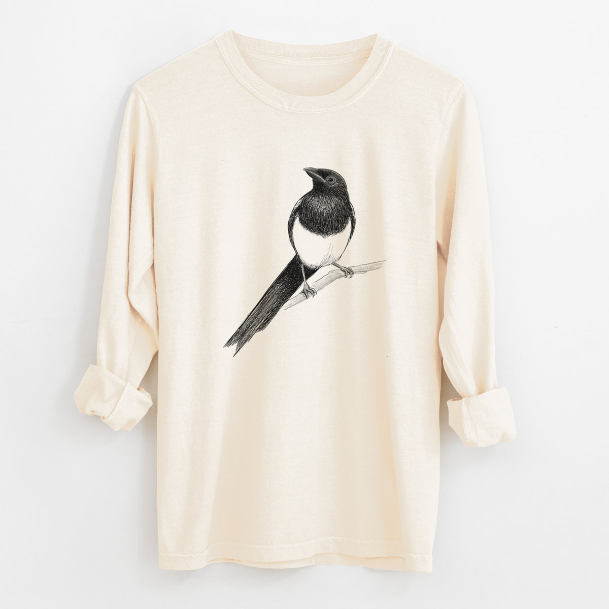 Ivory Comfort Colors long sleeve shirt laid flat with the cuffs rolled, printed with a detailed black ink sketch of a black-billed magpie perched on a branch with its long tail.