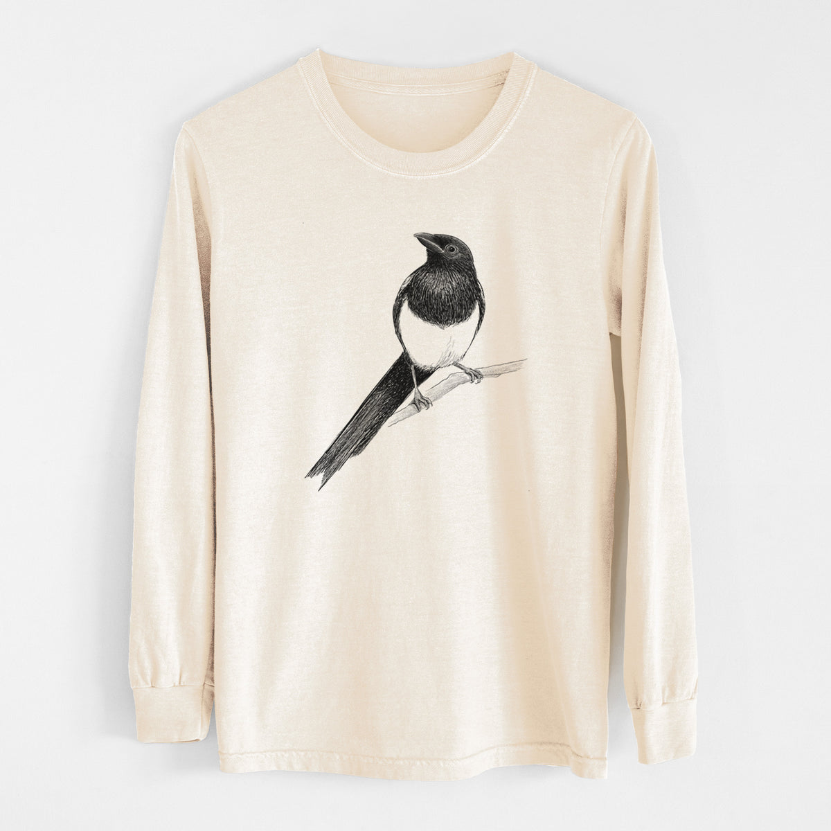 Ivory Comfort Colors long sleeve shirt laid flat, printed with a detailed black ink sketch of a black-billed magpie perched on a branch with its long tail.