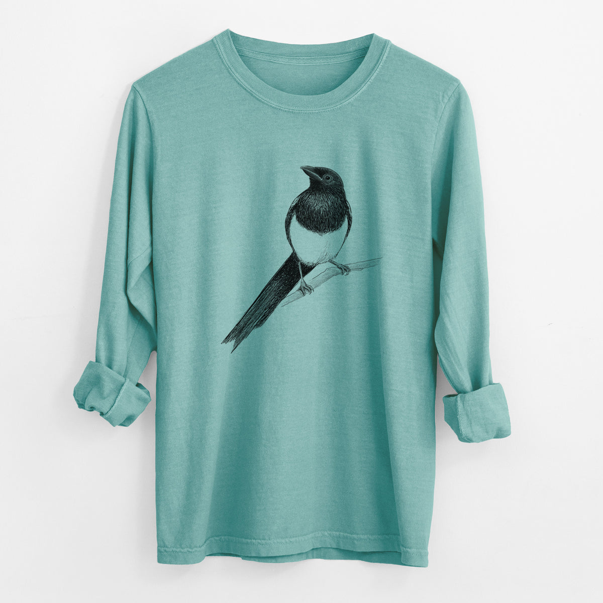 Reef green Comfort Colors long sleeve shirt laid flat with the cuffs rolled, printed with a detailed black ink sketch of a black-billed magpie perched on a branch with its long tail.