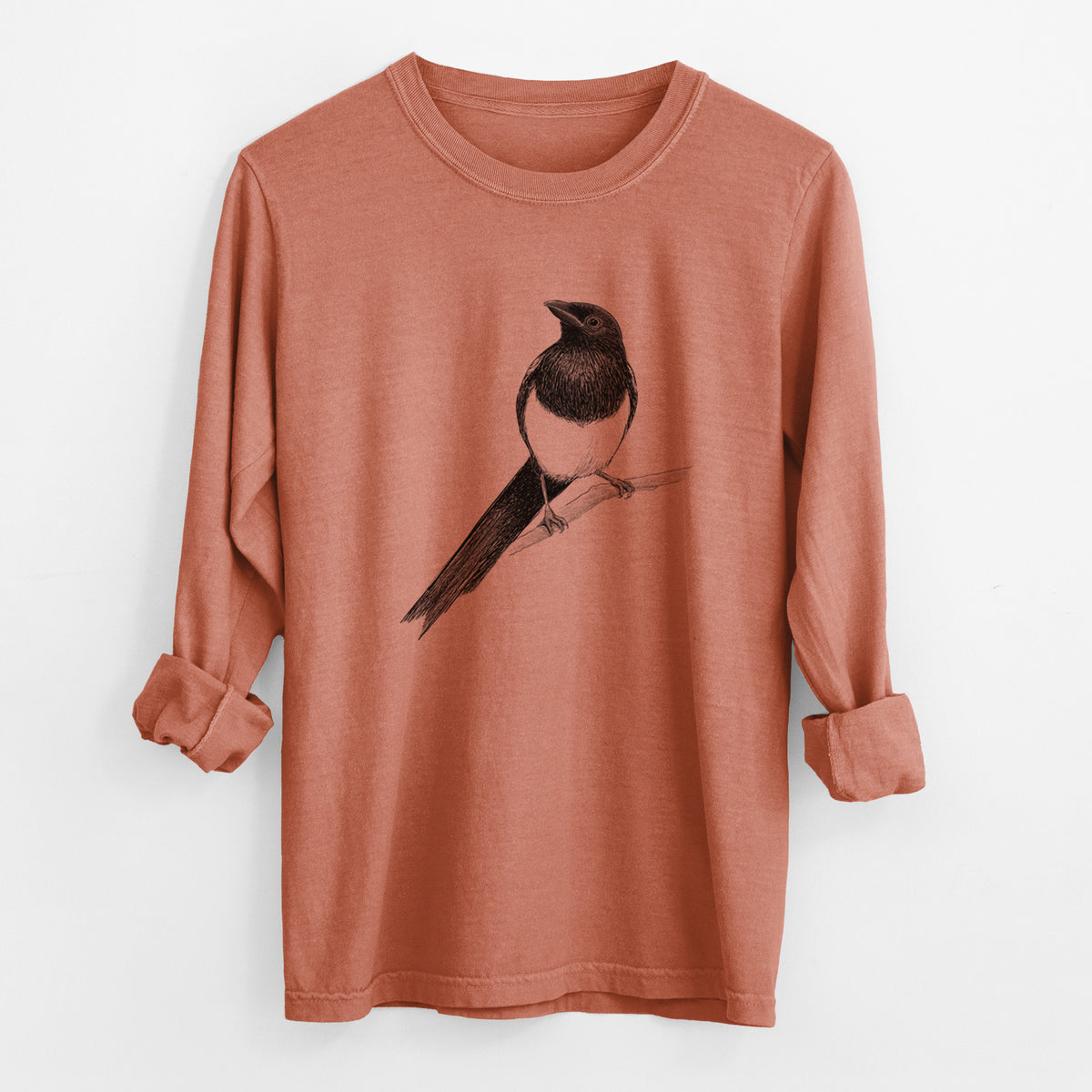Yam burnt orange Comfort Colors long sleeve shirt laid flat with the cuffs rolled, printed with a detailed black ink sketch of a black-billed magpie perched on a branch with its long tail.