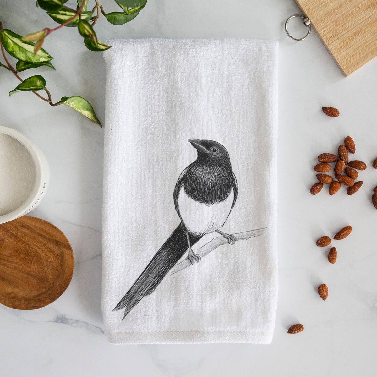 White hand towel printed with a detailed black ink sketch of a black-billed magpie perched on a branch with its long tail.