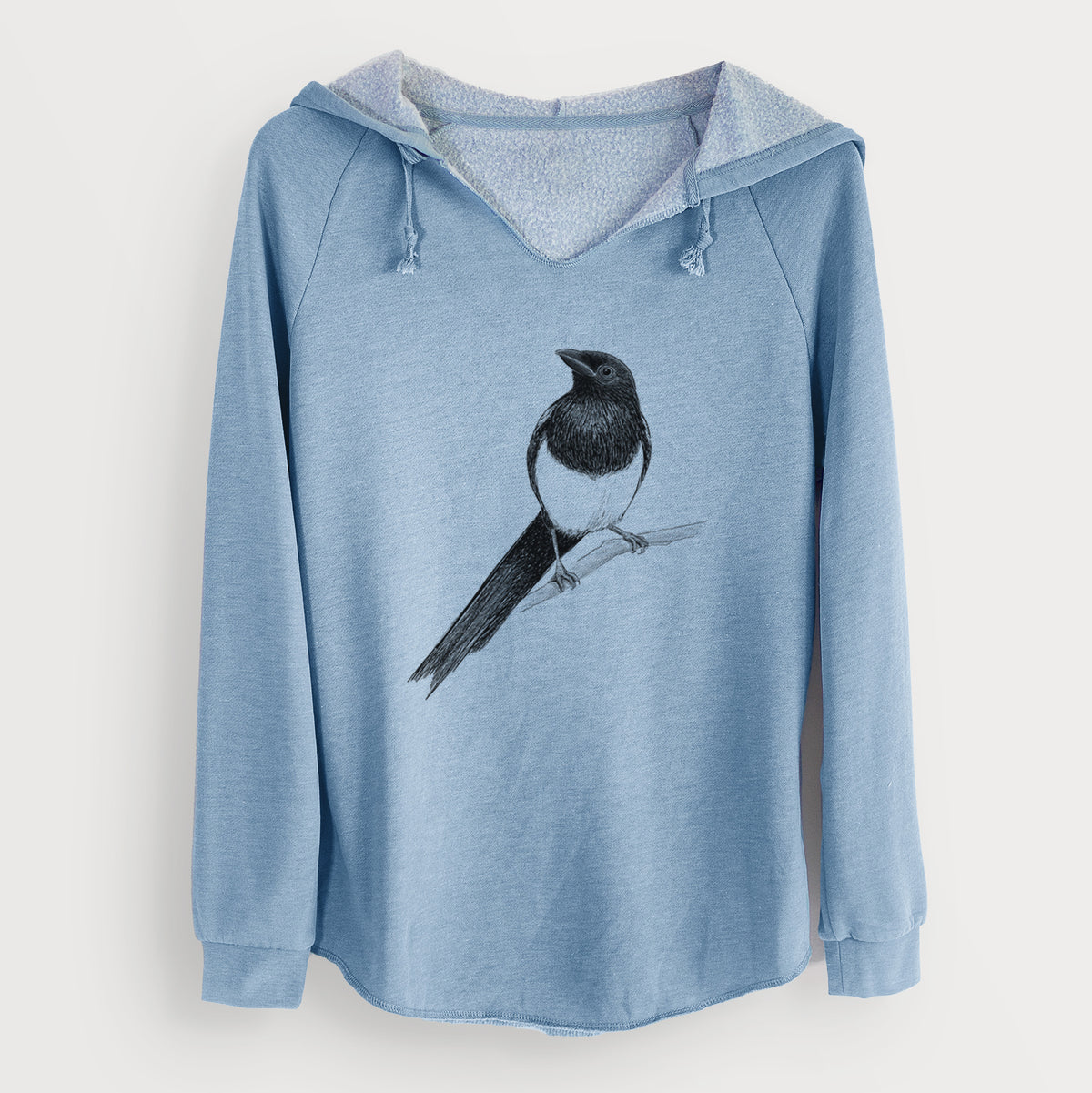 Misty blue women's Cali Wave hooded sweatshirt laid flat, printed with a detailed black ink sketch of a black-billed magpie perched on a branch with its long tail.