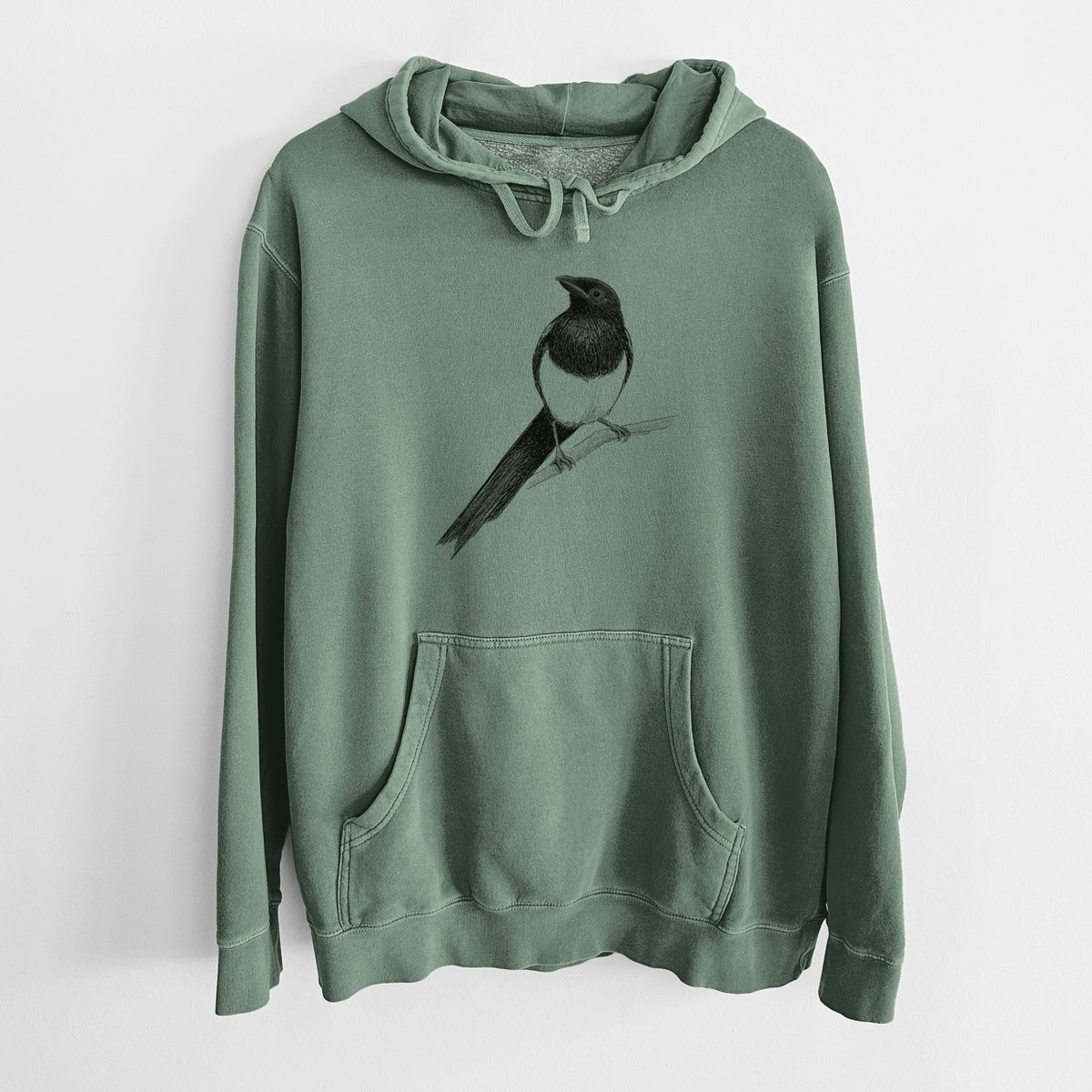 Alpine green pigment dyed hoodie laid flat, printed with a detailed black ink sketch of a black-billed magpie perched on a branch with its long tail.