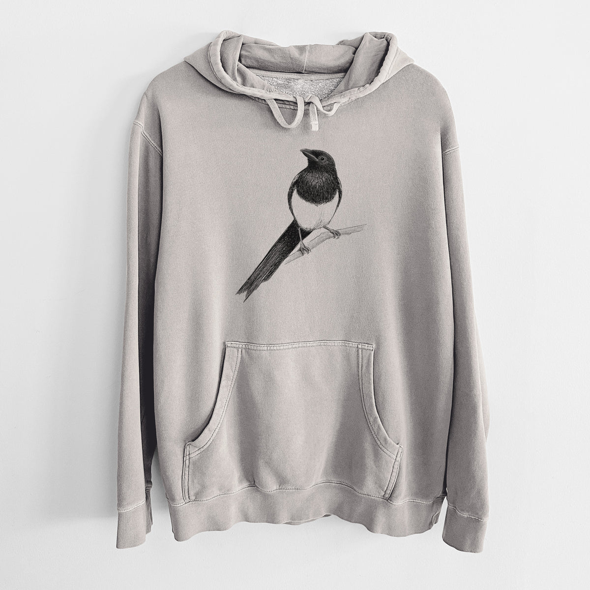 Cement grey pigment dyed hoodie laid flat, printed with a detailed black ink sketch of a black-billed magpie perched on a branch with its long tail.