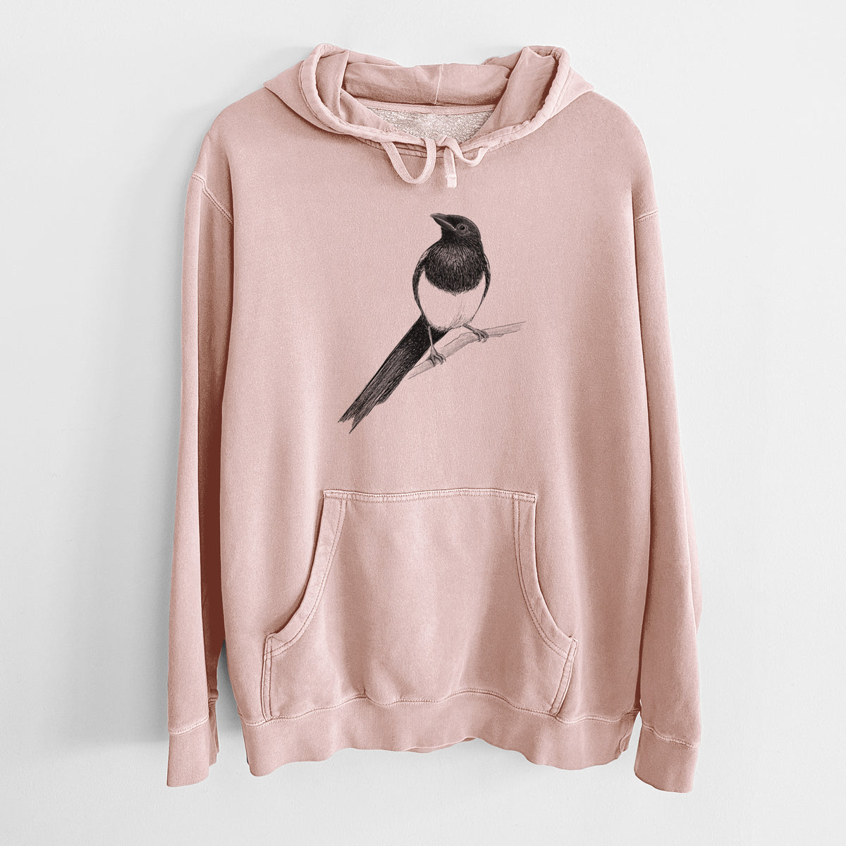 Dusty pink pigment dyed hoodie laid flat, printed with a detailed black ink sketch of a black-billed magpie perched on a branch with its long tail.
