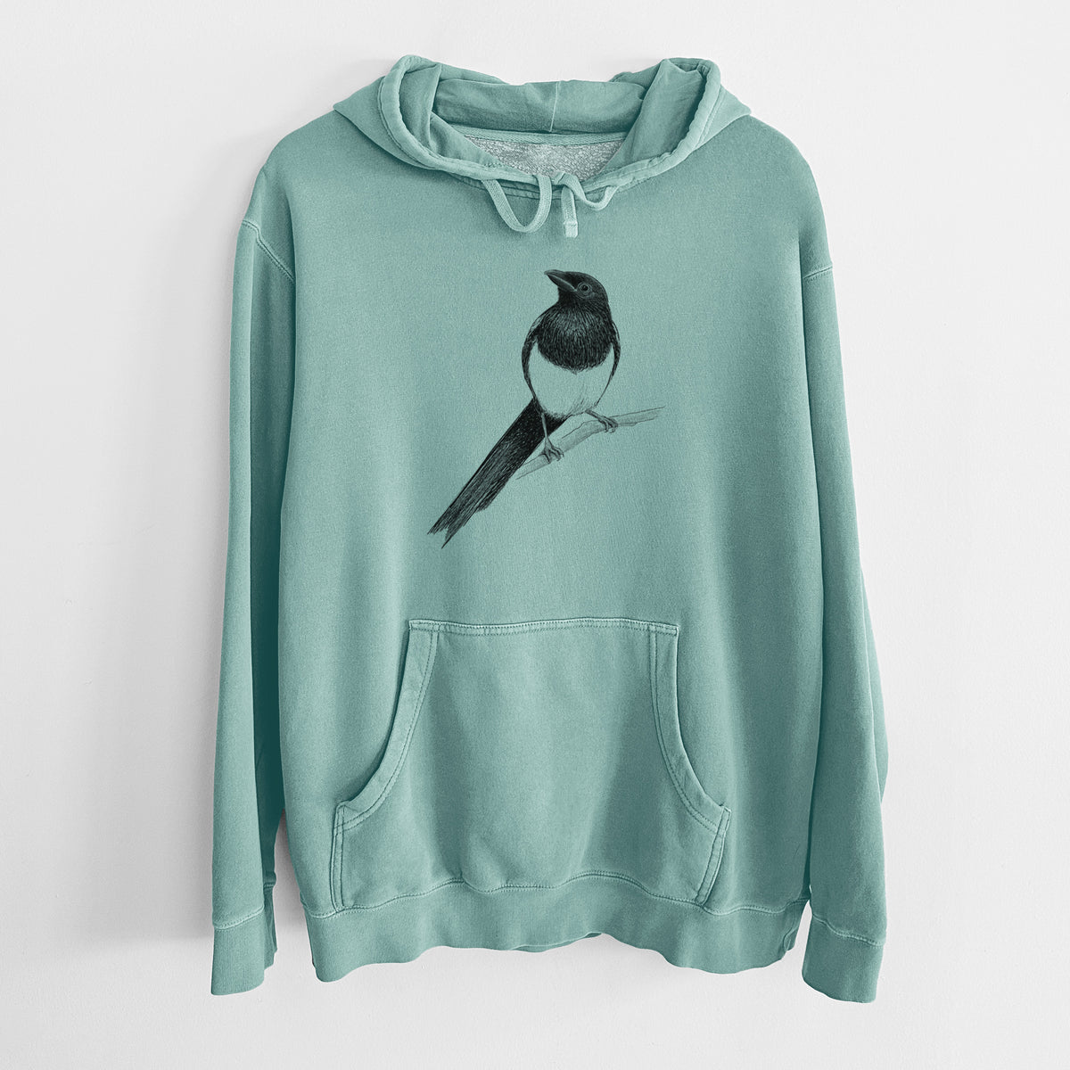 Mint green pigment dyed hoodie laid flat, printed with a detailed black ink sketch of a black-billed magpie perched on a branch with its long tail.