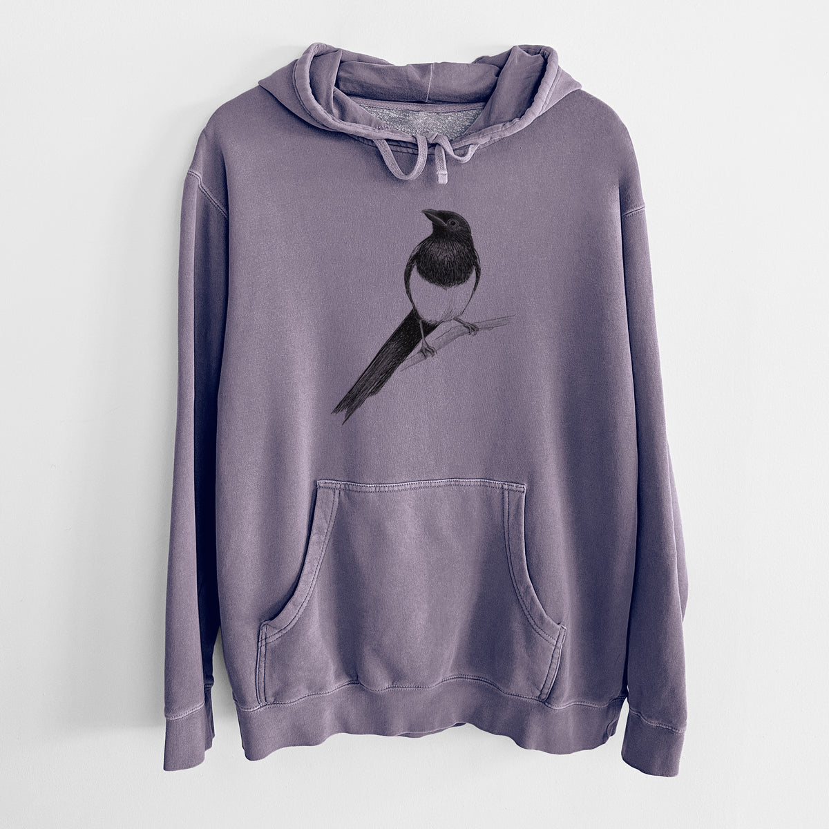 Plum purple pigment dyed hoodie laid flat, printed with a detailed black ink sketch of a black-billed magpie perched on a branch with its long tail.