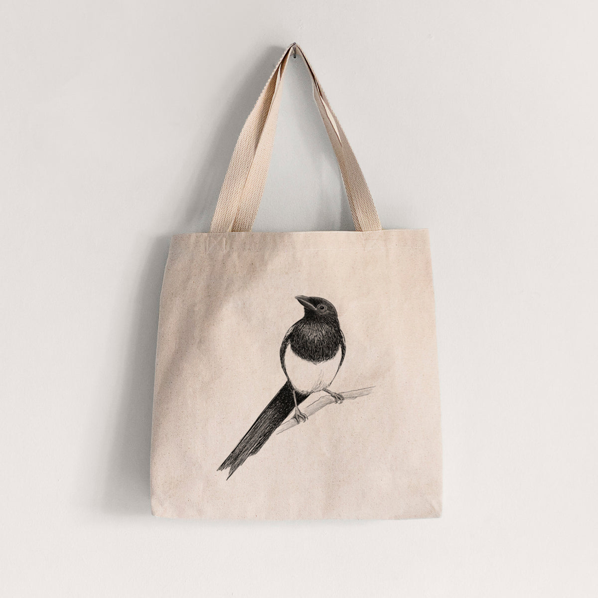 Natural canvas tote bag printed with a detailed black ink sketch of a black-billed magpie perched on a branch with its long tail.