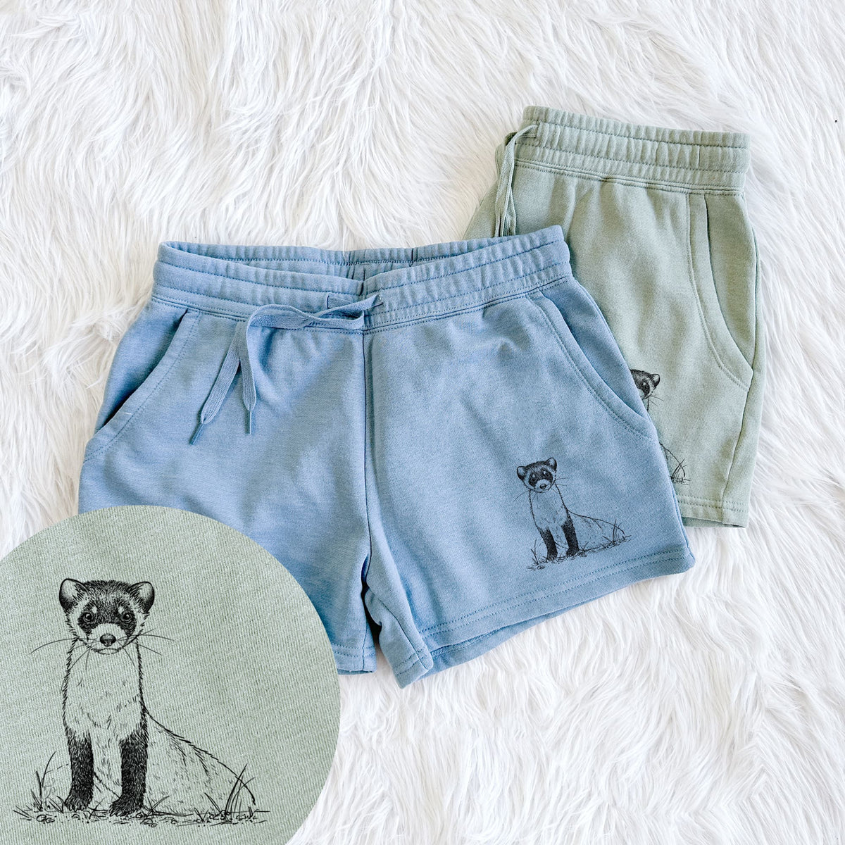 Two pairs of Cali Wave shorts in different colors printed with a detailed black ink illustration of a black-footed ferret sitting on the ground, with a close-up of the print.