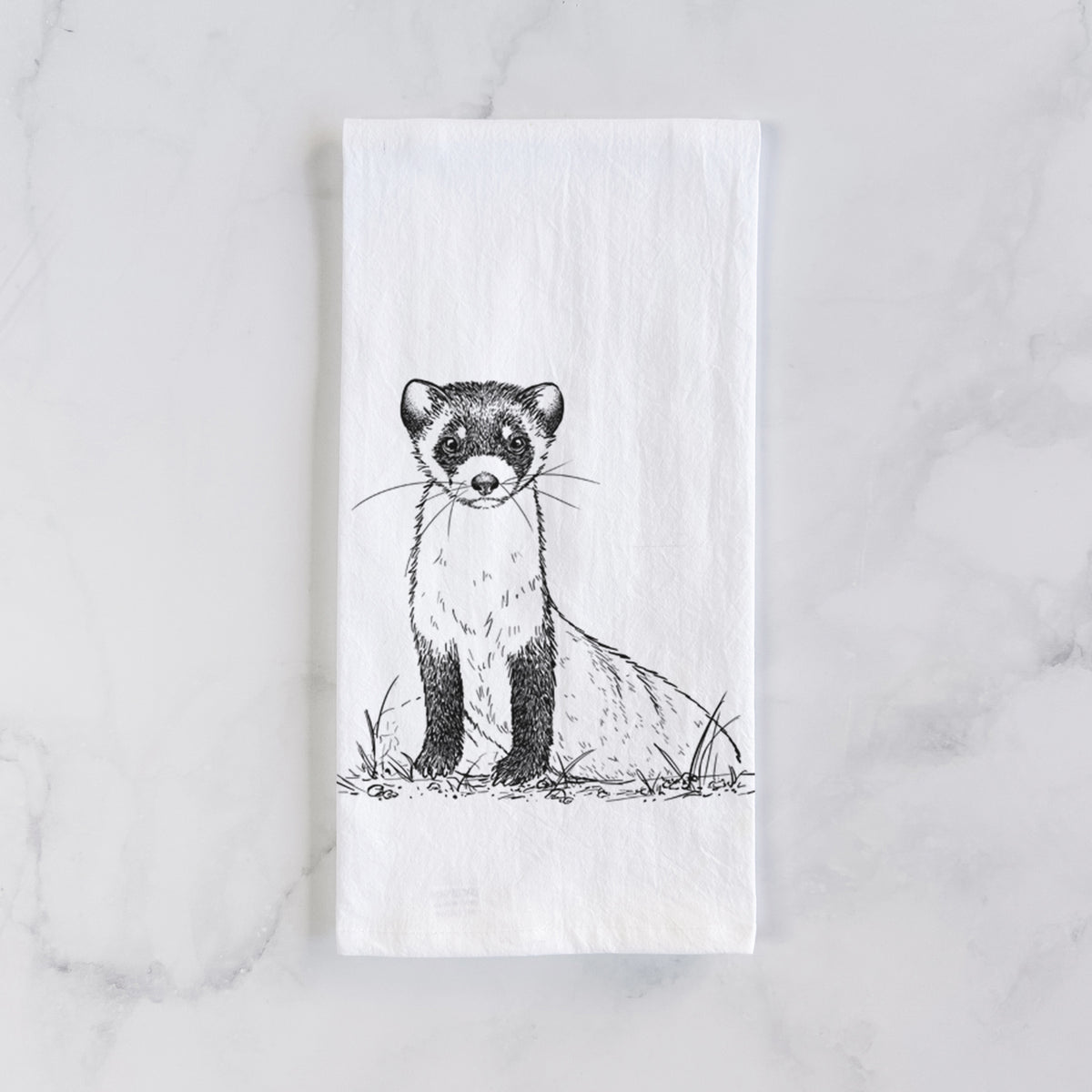 White cotton tea towel laid flat on marble, printed with a detailed black ink illustration of a black-footed ferret sitting on the ground.