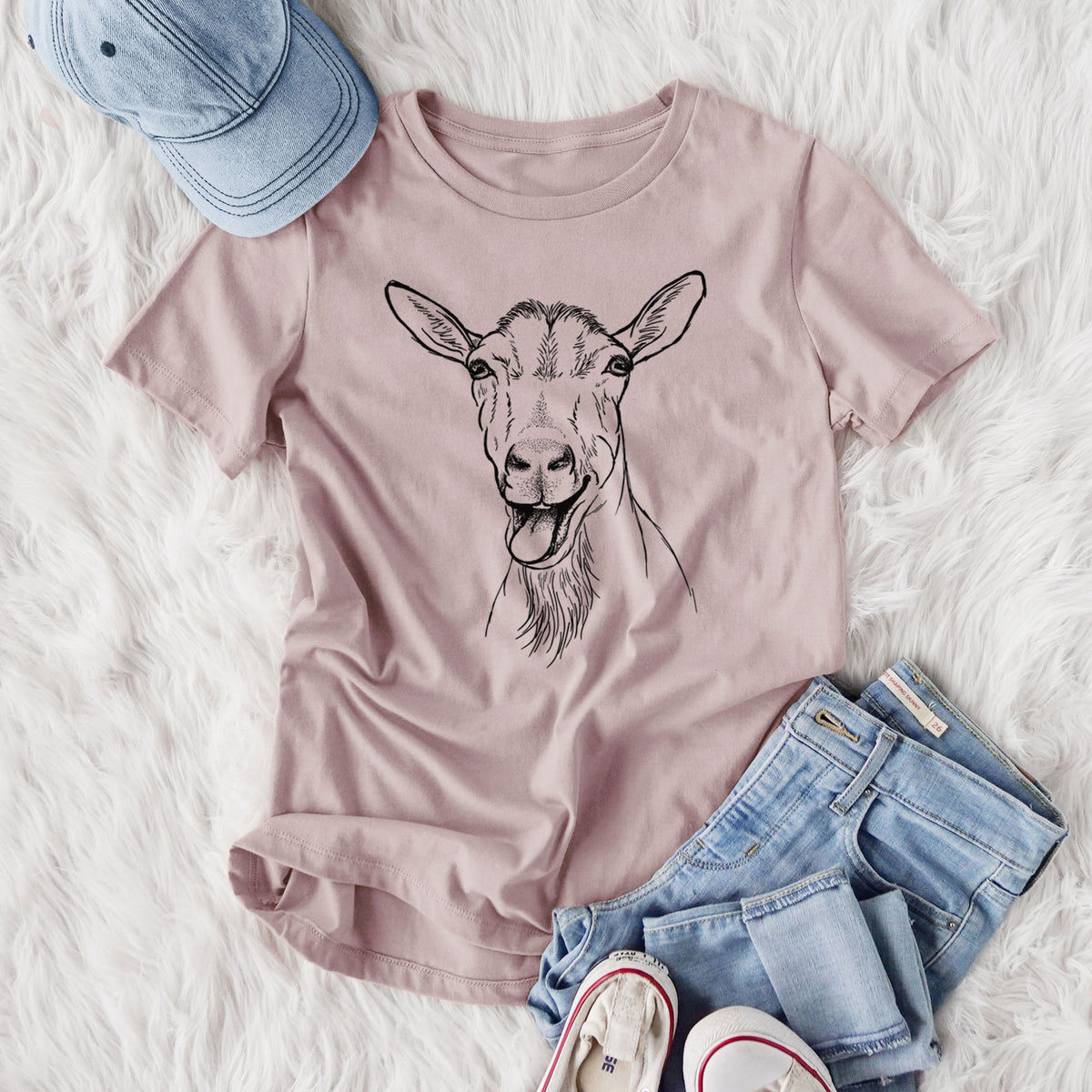 Women's relaxed fit cotton t-shirt printed with a black ink illustration of a goat's head with its mouth open mid-bleat and its tongue out, styled flat on a white faux fur rug with jeans.