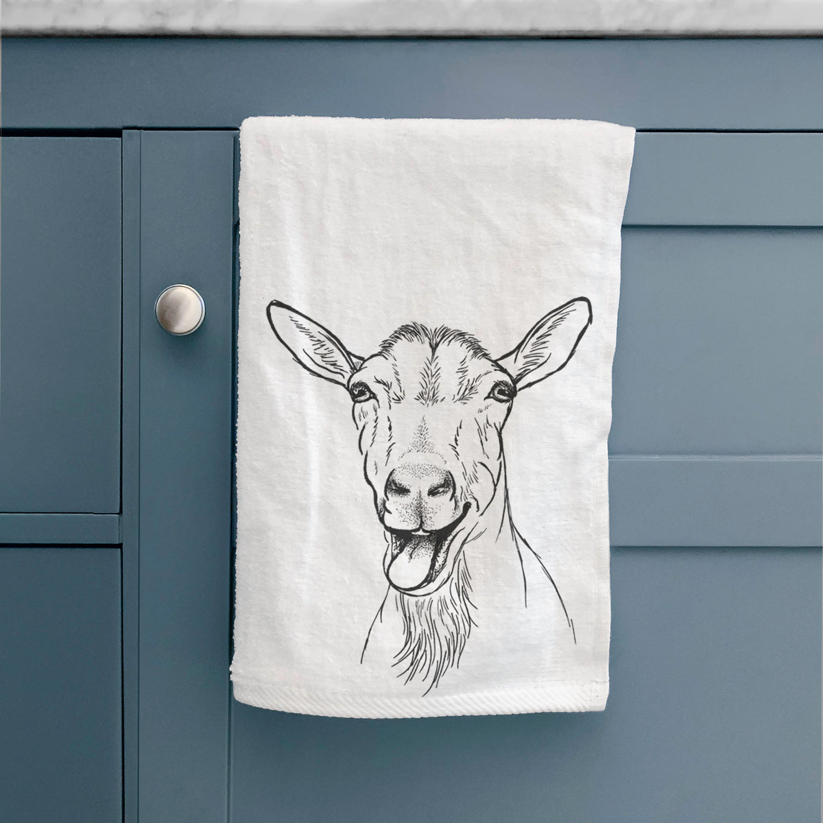 White hand towel printed with a black ink illustration of a goat's head with its mouth open mid-bleat and its tongue out, hanging on a cabinet door.