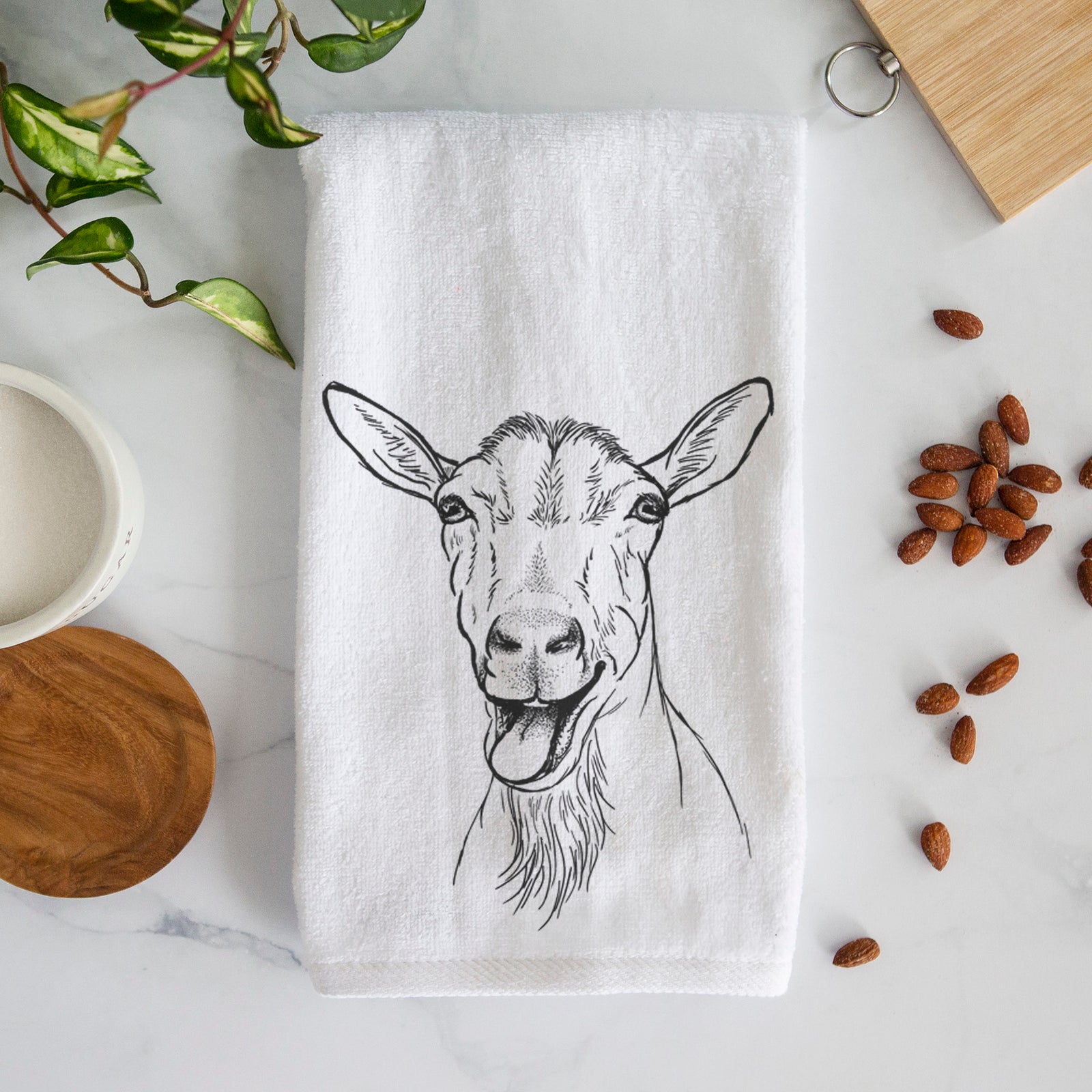 White hand towel printed with a black ink illustration of a goat's head with its mouth open mid-bleat and its tongue out.
