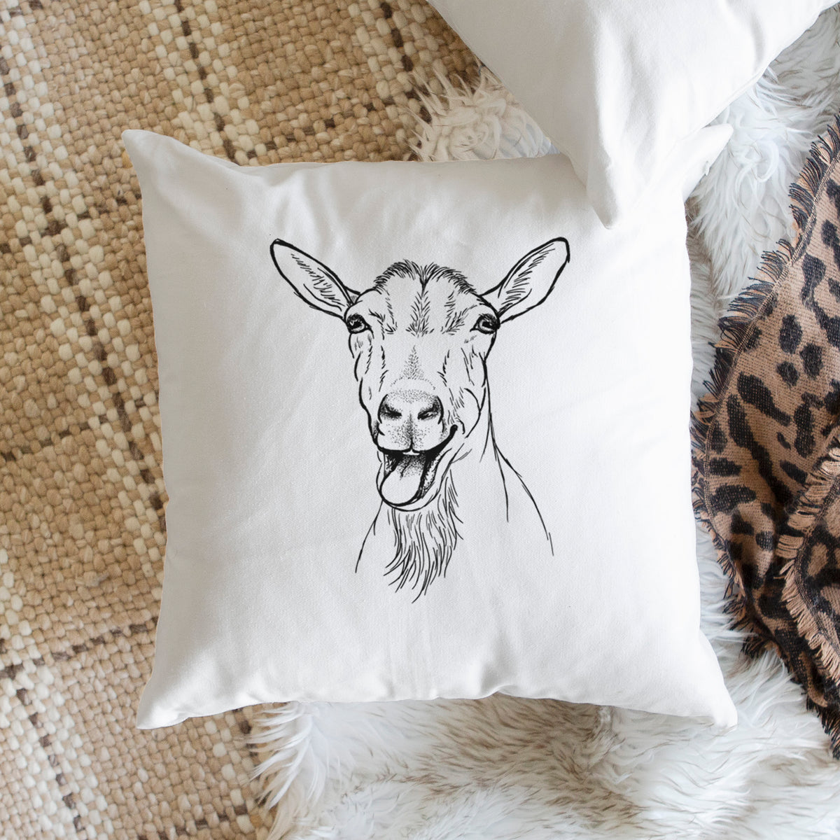 White pillow cover printed with a black ink illustration of a goat's head with its mouth open mid-bleat and its tongue out, on a woven chair.