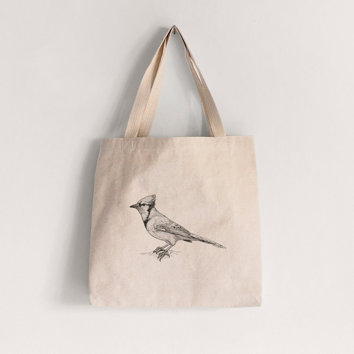 Natural canvas tote bag printed with a detailed black ink sketch of a blue jay perched with its crest raised.