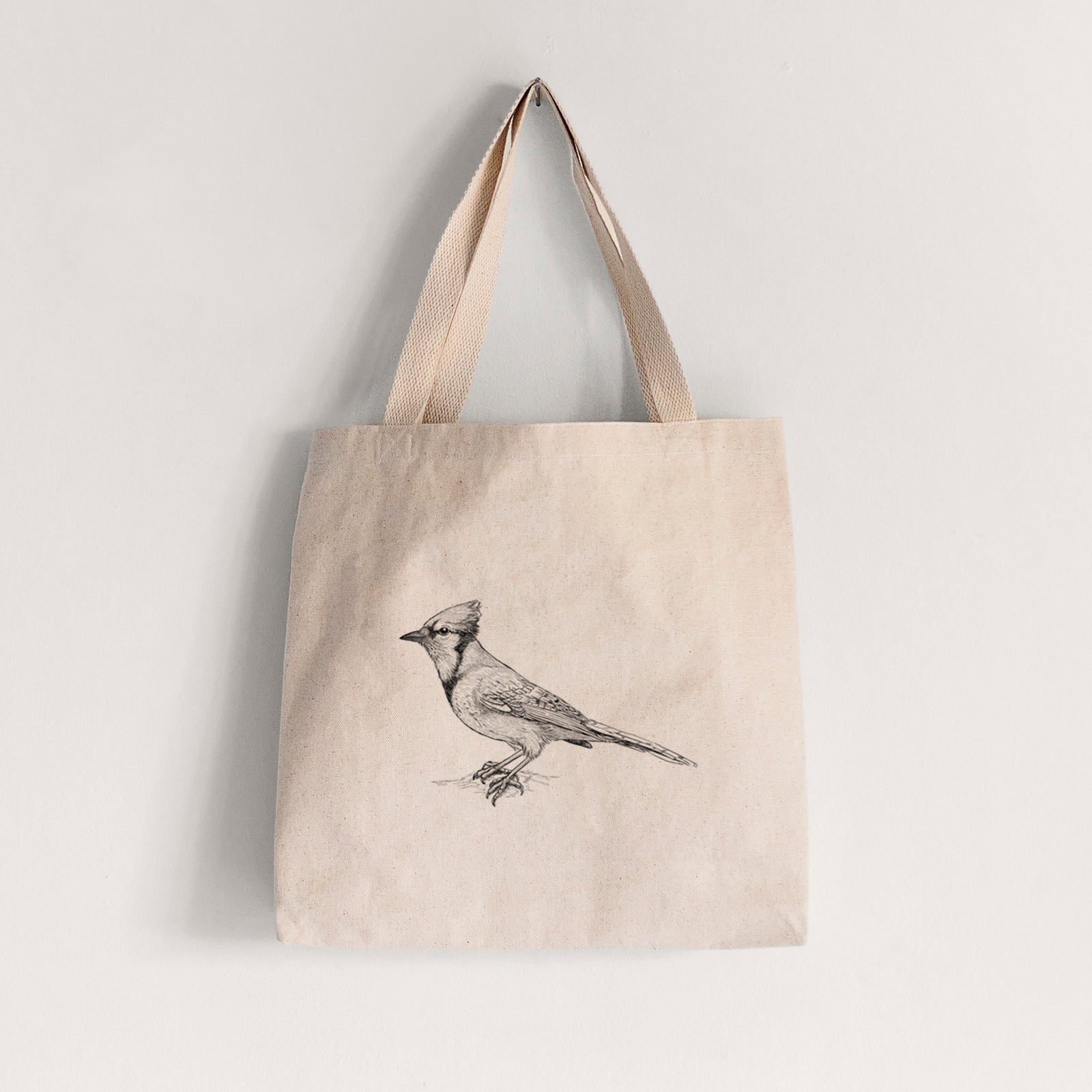 Natural canvas tote bag printed with a detailed black ink sketch of a blue jay perched with its crest raised.