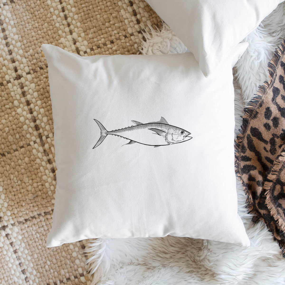 White pillow cover printed with a black ink line drawing of a bluefin tuna swimming, on a woven chair.