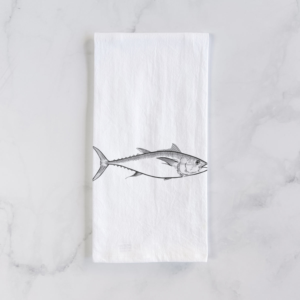 White cotton tea towel laid flat on marble, printed with a black ink line drawing of a bluefin tuna swimming.