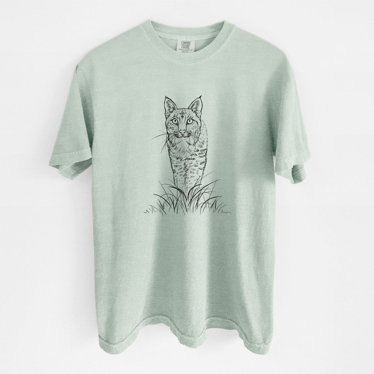 Bay green Comfort Colors t-shirt laid flat, printed with a black ink illustration of a bobcat standing in tall grass, facing forward.