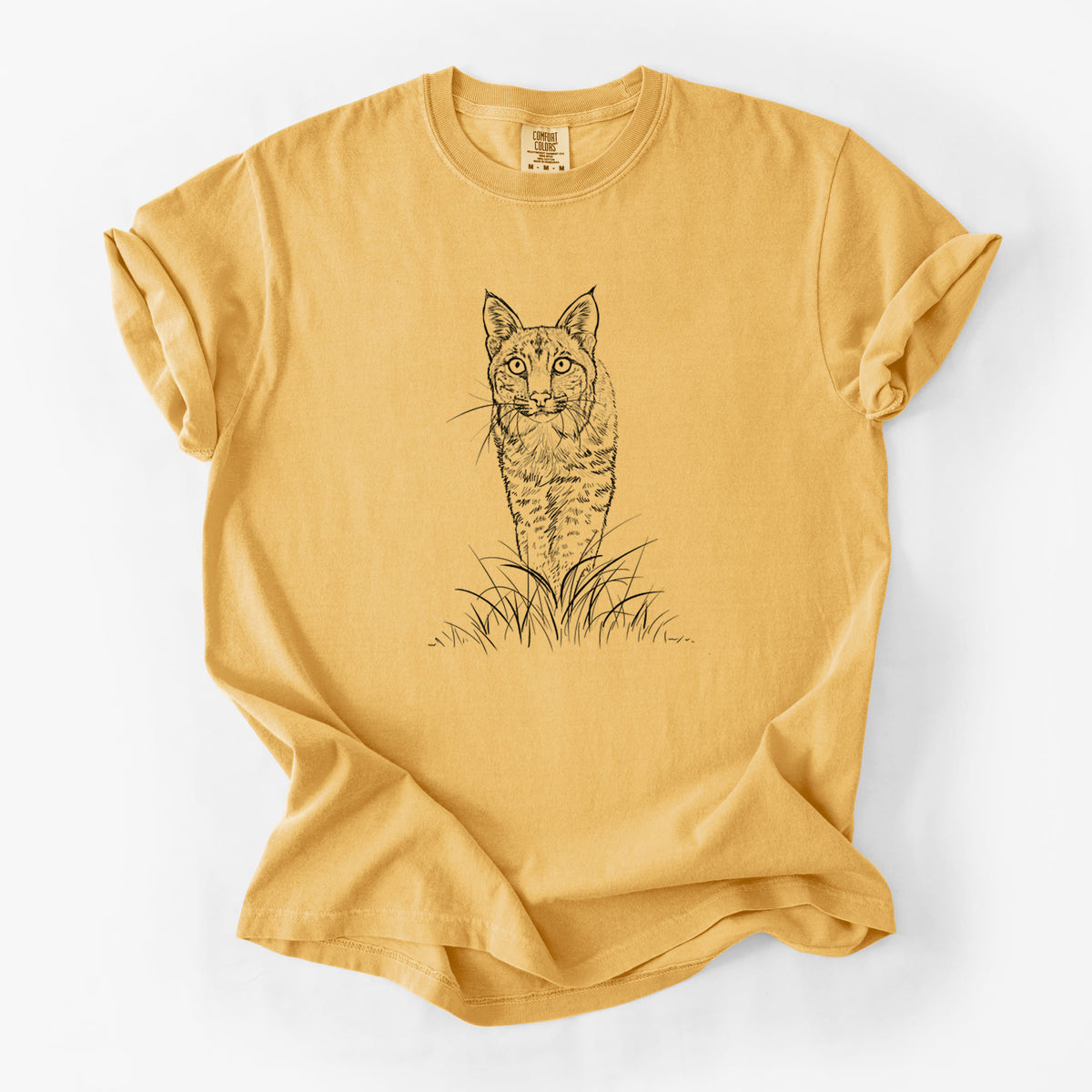 Golden wheat yellow Comfort Colors t-shirt laid flat, printed with a black ink illustration of a bobcat standing in tall grass, facing forward.