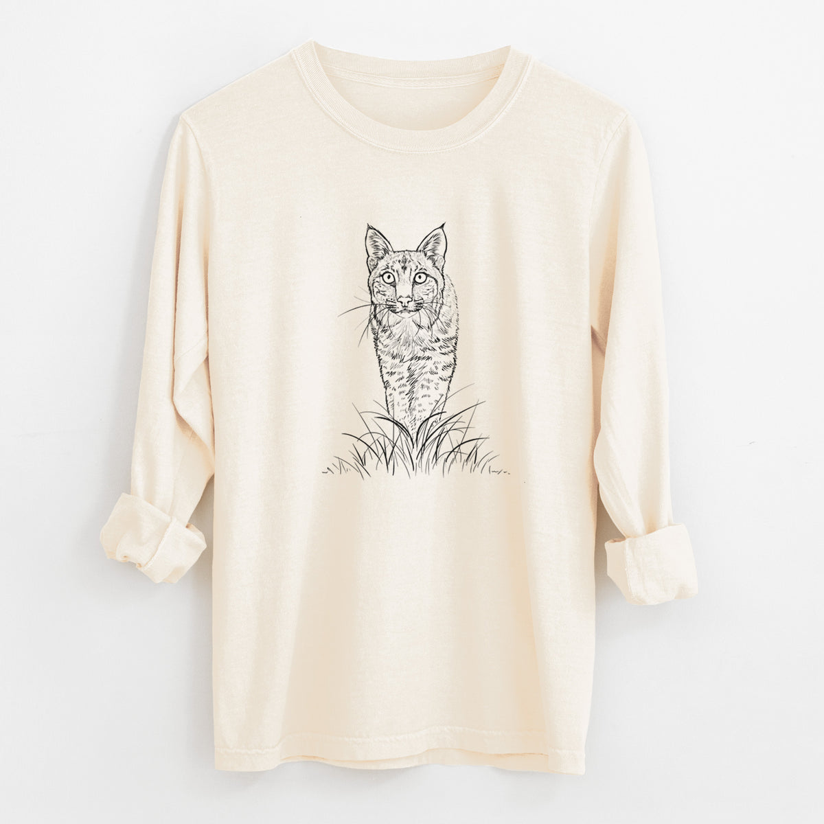Ivory Comfort Colors long sleeve shirt laid flat with the cuffs rolled, printed with a black ink illustration of a bobcat standing in tall grass, facing forward.